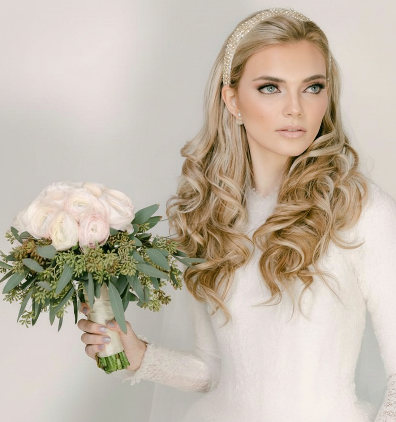A bride with long, waved hair, holding a bouquet.